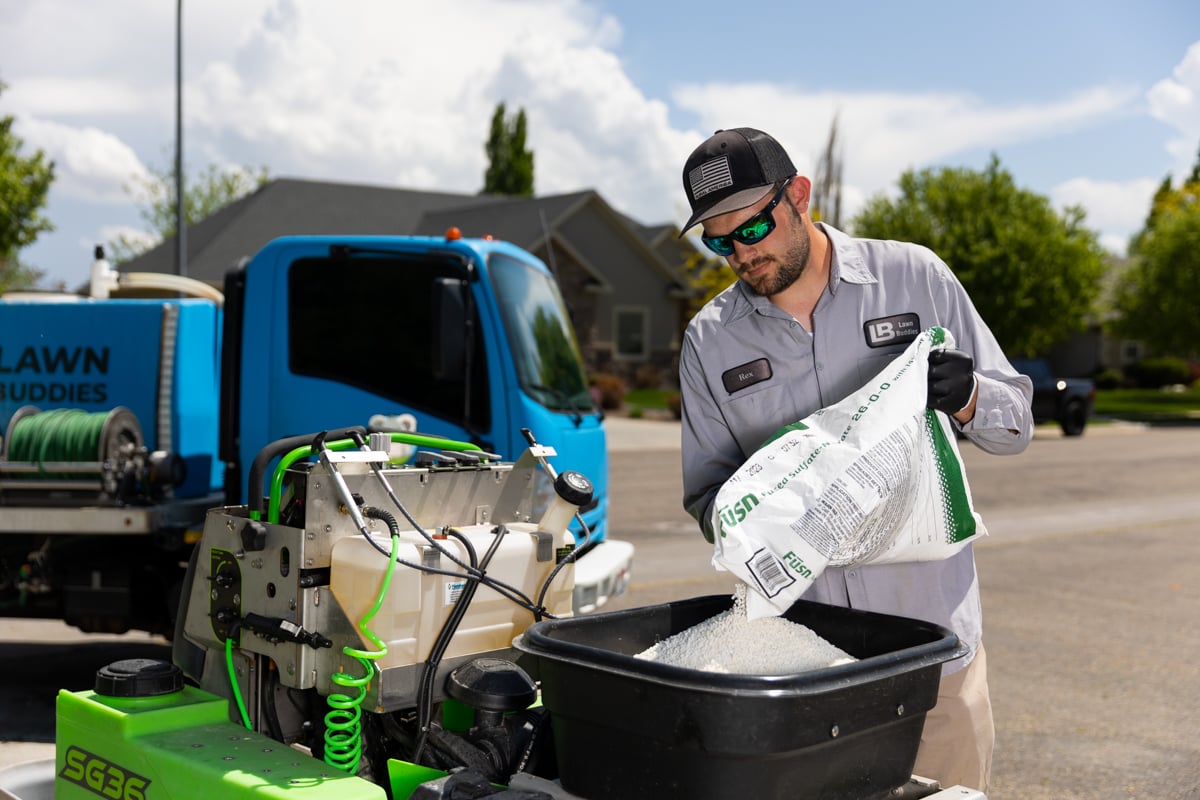 lawn care technician pours fertilizer into spreader