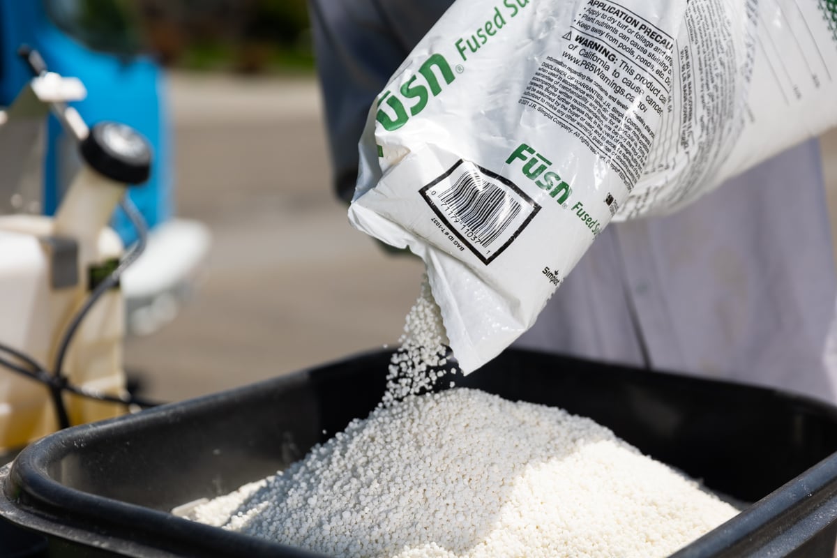 lawn care expert pours fertilizer in spreader