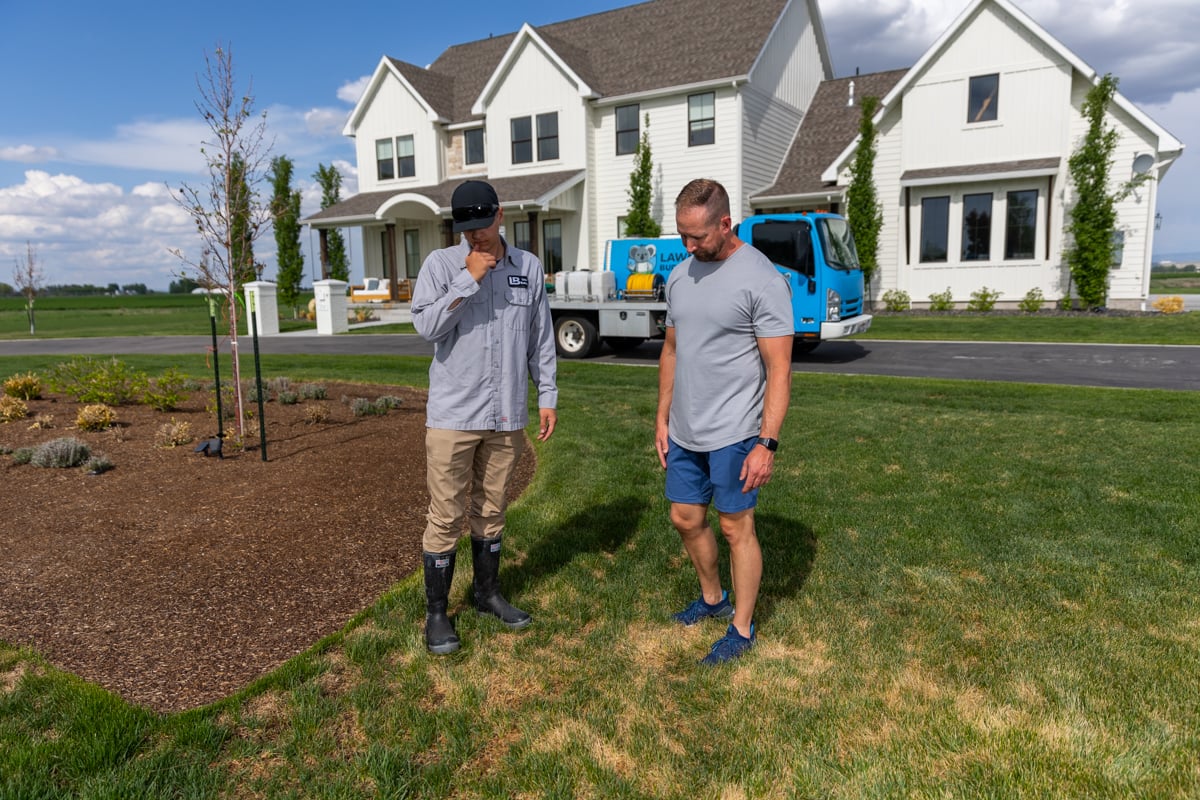 lawn care technician inspects grass with homeowner